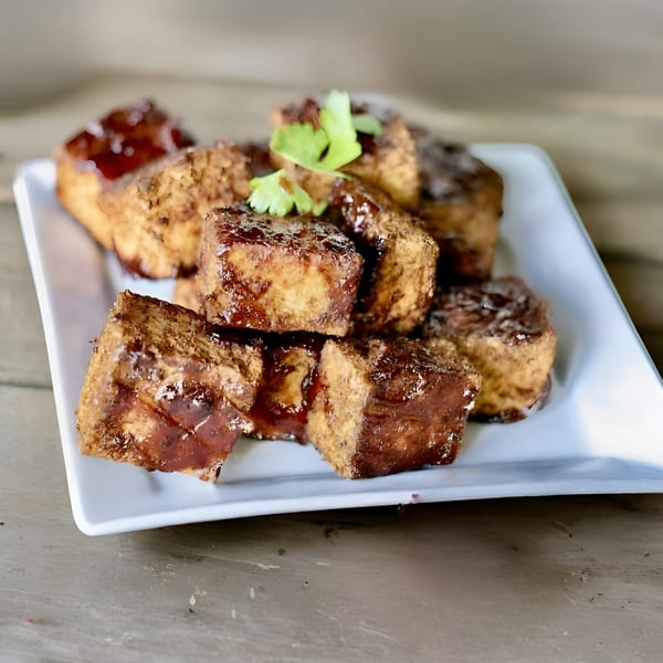Close-up of crispy fried tofu cubes glazed with a dark sauce and garnished with cilantro.