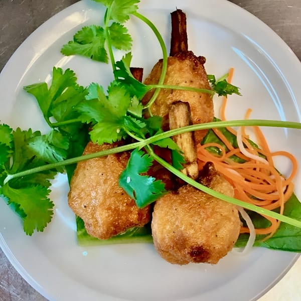 Three golden-brown fried shrimp paste on sugarcane, garnished with fresh cilantro and shredded carrots.