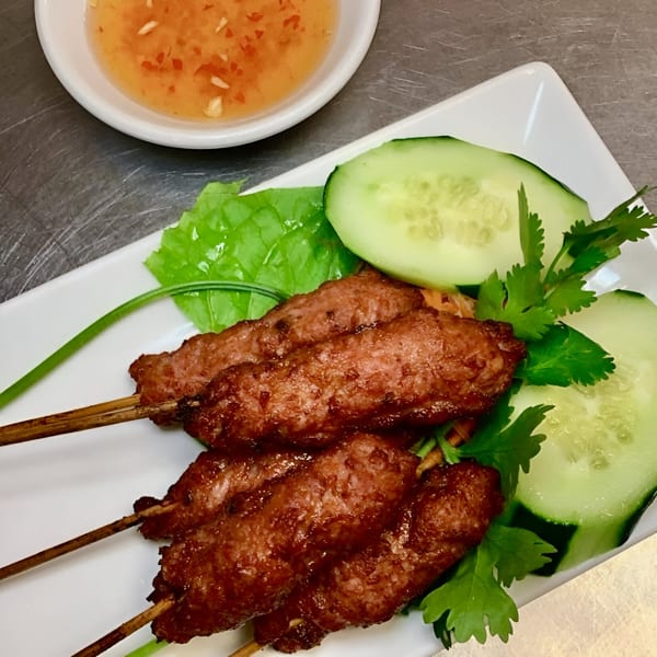 Vietnamese grilled pork skewers with fresh cucumber, lettuce, cilantro, and a side of dipping sauce.