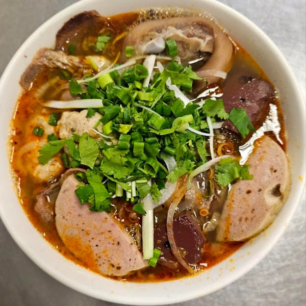 A close-up of a vibrant bowl of Vietnamese Bun Bo Hue soup, garnished with fresh herbs.