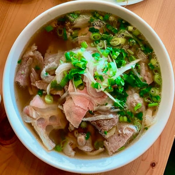 A large bowl of Pho 07 Vietnamese pho with beef, noodles, broth, and green onions.